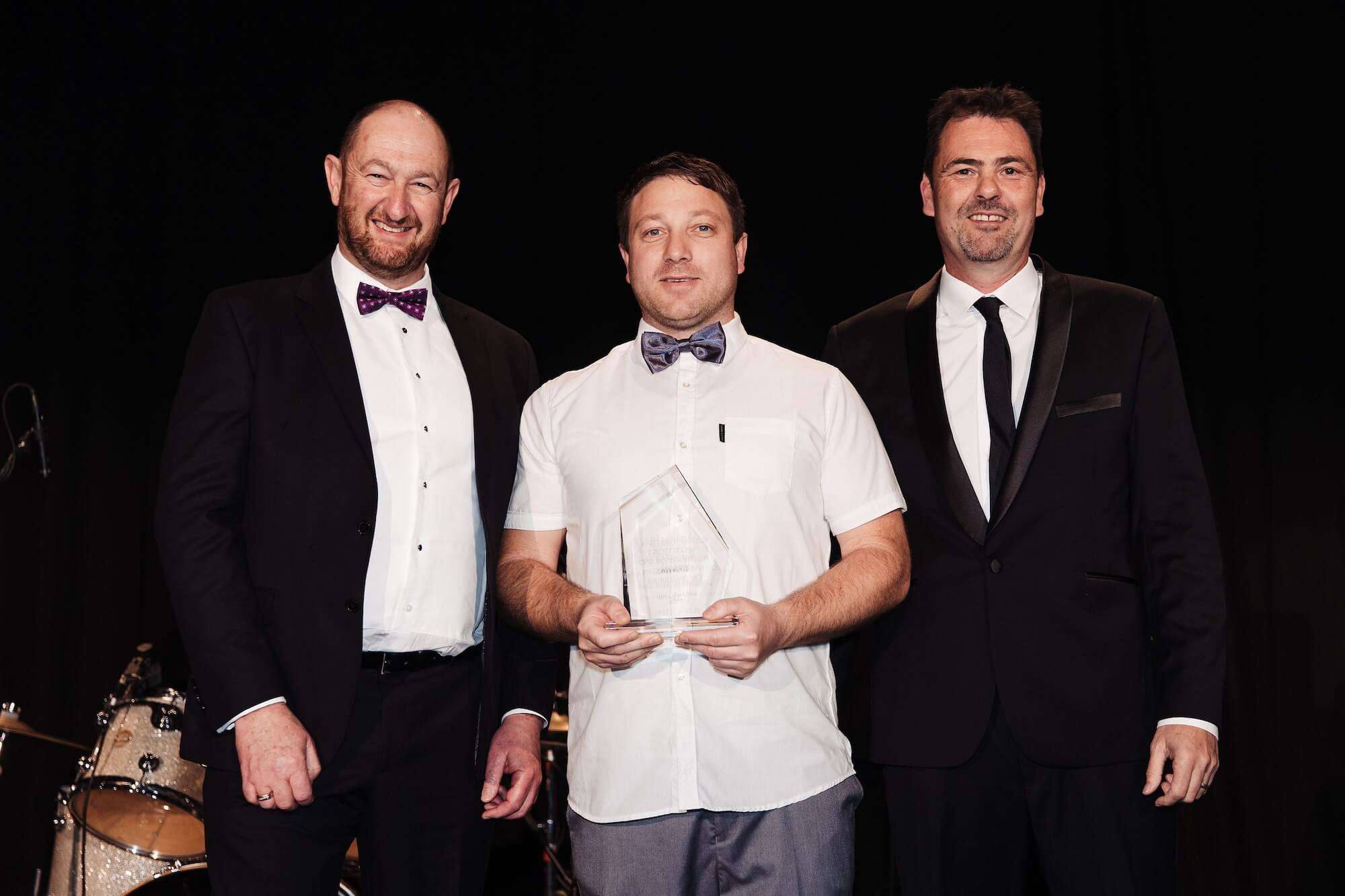 Three men standing next to each other holding an award.